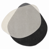 A modern abstract oval rug with a three-tone color-blocked design in cream, light gray, and black, shown on a plain white background.