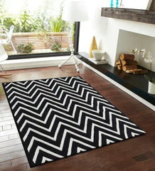 Black and white handwoven wool rug with tufted chevron pattern on wooden floor in modern living room