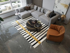 Modern living room with gray sectional sofa, orange armchair, striped black white rug with gold accent, and round coffee tables