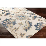 Hand-tufted Blumea rug with blue and beige floral design on cream background, displayed on dark hardwood floor