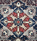 Close-up of a burgundy vintage style handwoven rug with geometric and floral patterns in navy, gray, and cream