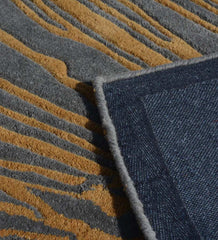 Close-up of charcoal gray and golden brown abstract patterned rug with folded navy blue corner