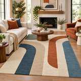 A large area rug with a mid-century modern abstract design in navy blue, terracotta orange, and cream beige, styled in a bright, contemporary living room.