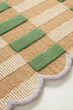 Close-up of luxury handwoven rug with green checkered and beige textured patterns and scalloped gray edge