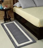 Grey hand-tufted wool runner rug with white border beside a bed and dark wood nightstand