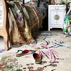 Luxury floral and bird patterned handwoven rug by Mannat Rugs with colorful throw and slippers in elegant living space