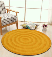 Mustard yellow round rug with concentric circle design on light wooden floor near plaid armchair and decorative pillow