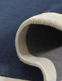 Close-up of a navy blue rug with a cream border rolled partially to show texture and thickness
