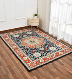 Orange and blue traditional hand-tufted rug on wooden floor beside beige stool with plant and book near sheer curtains