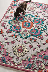 Persian-inspired medallion rug with vibrant teal, orange, and pink floral patterns on beige and magenta background, with a black cat walking on it