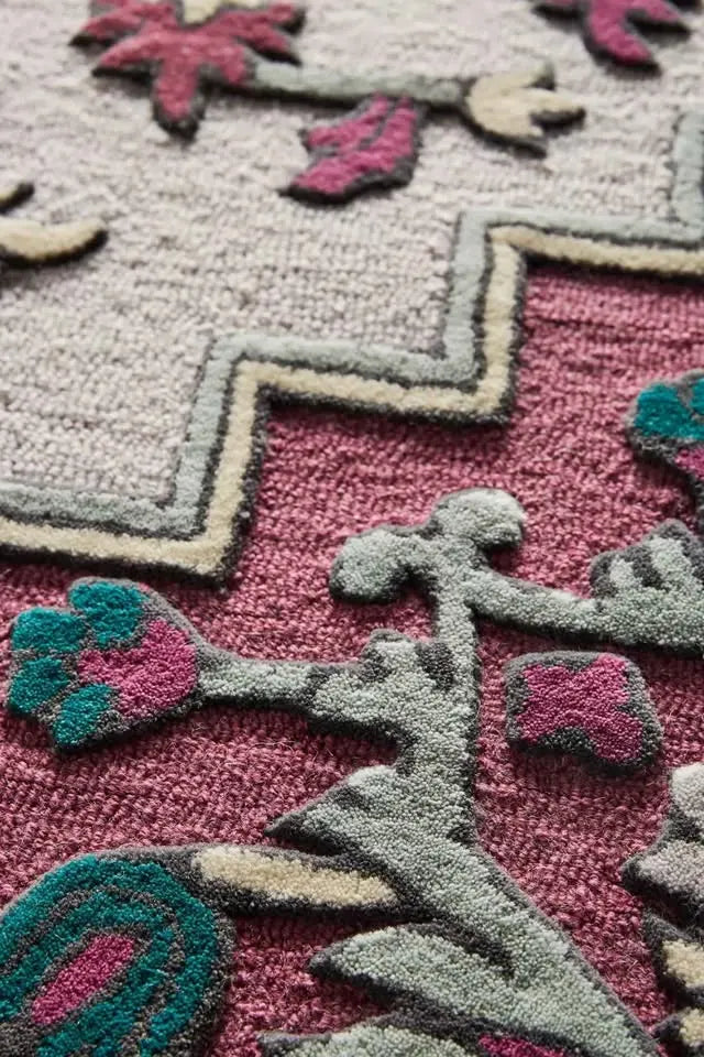 Close-up of a textured rug with geometric patterns in pink, gray, and green.
