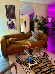 Modern living room with a brown sofa, clear coffee table, and colorful decor.