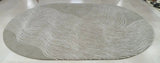 Round gray rug with wavy white lines on a white floor.