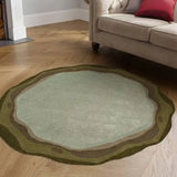 Round sage green and earthy tone rug with wavy border on wooden floor beside beige tufted sofa
