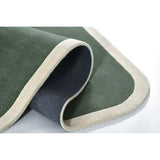 Sage green rectangular rug with cream border, partially rolled to show dark backing