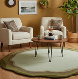 Living room with sage green round area rug, two beige armchairs, wooden coffee table, and earth tone decor