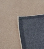 Corner of a solid beige hand-tufted rug showing textured dark gray backing on beige floor