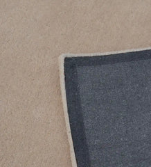 Corner of a solid beige hand-tufted rug showing textured dark gray backing on beige floor