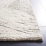 Close-up of a hand-tufted wool rug with textured, wave-like patterns in light beige and gray tones on a dark hardwood floor