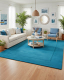 Teal blue solid area rug with a clean border frame design, hand-tufted texture adding a refined, modern, and calming accent to the interior space in living room.