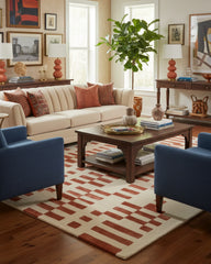 Terracotta and beige geometric area rug in a stylish living room with cream sofa, blue chairs, wood coffee table, and decorative accents