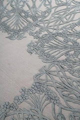 Close-up of a luxury hand-tufted rug from Mannat Rugs with intricate raised floral and vine patterns in muted gray tones