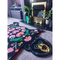 Black bear-shaped rug with colorful floral patterns on beige carpet by fireplace with plants