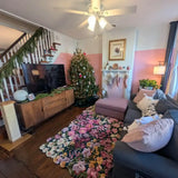 Cozy living room with floral luxury rug, pink accent wall, decorated Christmas tree, gray sofa with pink pillows, and fireplace with stockings