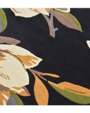Close-up of luxury handwoven rug with cream, orange, green, and brown floral pattern on black background