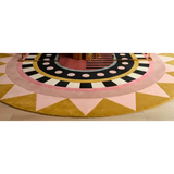 Round luxury rug with geometric design featuring pink, yellow, black, and white patterns on hardwood floor