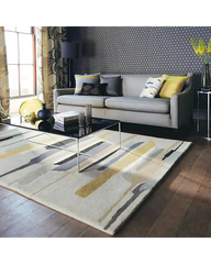 Modern living room with abstract patterned rug in beige, gold, and gray, gray sofa, decorative pillows, and geometric wallpaper