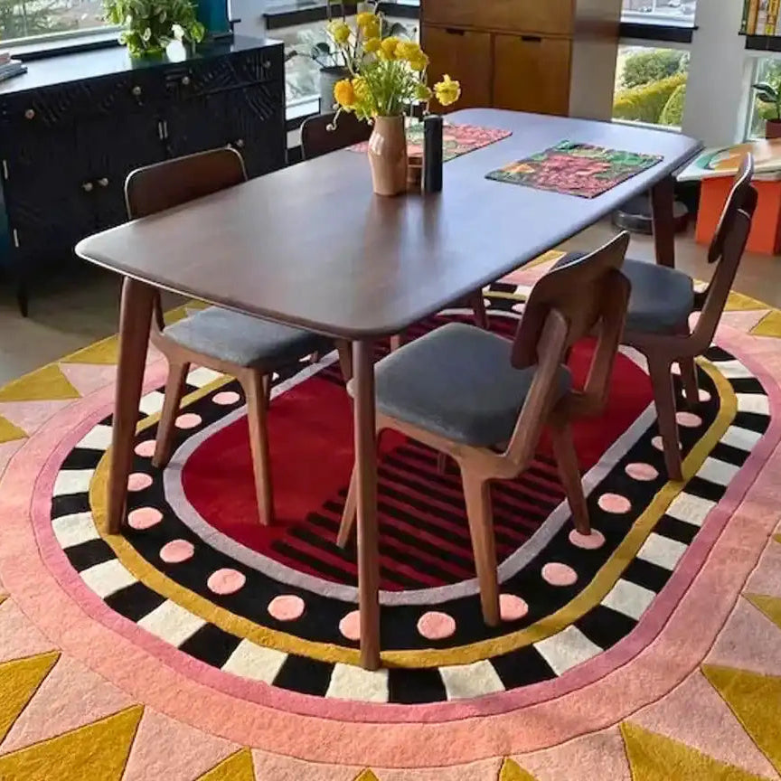 Modern dining room with wooden table, four chairs on a colorful geometric rug featuring red, pink, black, and mustard tones