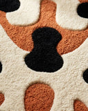 Close-up of a textured rug with black, orange, and white abstract pattern