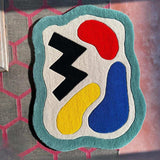 Abstract modern rug with wavy teal border and colorful red, blue, yellow, and black shapes on cream background