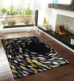 Black hand-tufted wool rug with abstract swirling leaf pattern in yellow, gray, and white on hardwood floor in modern living room