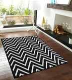 Black and white handwoven wool rug with tufted chevron pattern on wooden floor in modern living room
