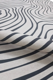 Close-up of a luxury black and white modern abstract wavy line rug, partially rolled up