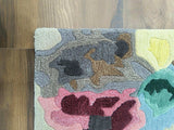 Hand-tufted wool rug with abstract patterns in gray, pink, yellow, green, and brown on wooden floor