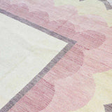 Close-up of handwoven blush pink scalloped rug with gray border and soft yellow accents