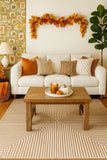 Cozy living room with a cream sofa, geometric striped rug, wooden coffee table, fall decor, and green fiddle leaf fig