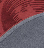 Close-up of burgundy round rug with raised ornate pattern and grey woven backing