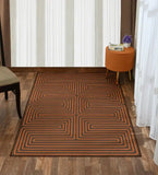 Burnt orange maze pattern rug on wooden floor with orange ottoman and purple flowers