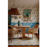 Cozy dining room with wooden table, wicker chairs, floral wallpaper, and soft yellow patterned rug