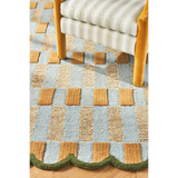 Luxury handwoven yellow and blue checkered rug with green scalloped edge under striped chair legs