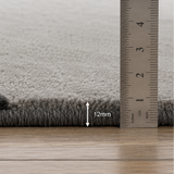 Close-up of a gray textured rug corner with a metal ruler showing a 12 mm pile height, placed on a light wood floor.