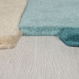 Close-up of two plush shag rugs, one in cream and one in light blue, shown on a light gray wood-look floor.