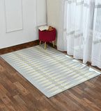 Modern diamond pattern rug in beige and yellow on wooden floor beside sheer curtains and red ottoman with book and cup