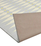 Handwoven luxury rug with diamond pattern in light gray, cream, and yellow, corner folded to show textured beige backing