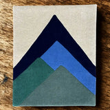 Abstract mountain peak rug with earthy green, blue, and navy shapes on beige background by Mannat Rugs