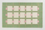 Handwoven luxury rug with green background, cream squares, and pink accents in geometric pattern
